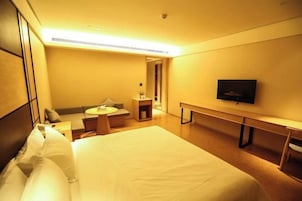 A hotel room with a large bed, a desk, a chair, a TV, and a small seating area with a sofa and a table.