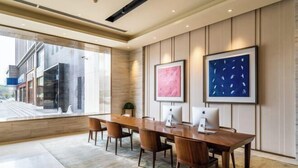 Een moderne vergaderruimte met een lange houten tafel, vier stoelen, twee Apple iMacs en kunstwerken in lijsten aan de muur.