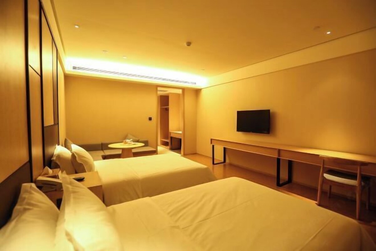 A hotel room with two beds, a desk, a chair, a television, and a small table.