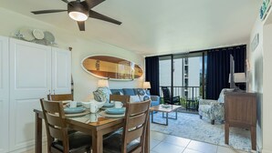 Uma sala de jantar com uma mesa posta para quatro pessoas, um ventilador de teto e uma prancha de surf na parede.