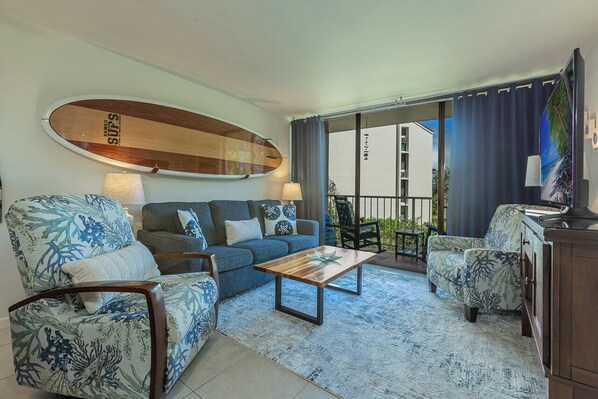 Una sala de estar con una tabla de surf, un sofá, dos sillones, una mesa de centro y vistas al exterior.