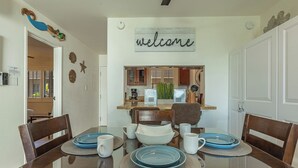 Uma área de refeições com uma mesa de vidro, pratos azuis, tigelas brancas e um letreiro com a palavra 'welcome' na parede.