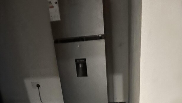 Una cocina con refrigerador, piso de baldosas y toma de corriente.
