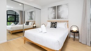 Une chambre d’hôtel moderne avec un grand lit, une table de chevet, une chaise, un miroir et des œuvres d’art accrochées au mur.