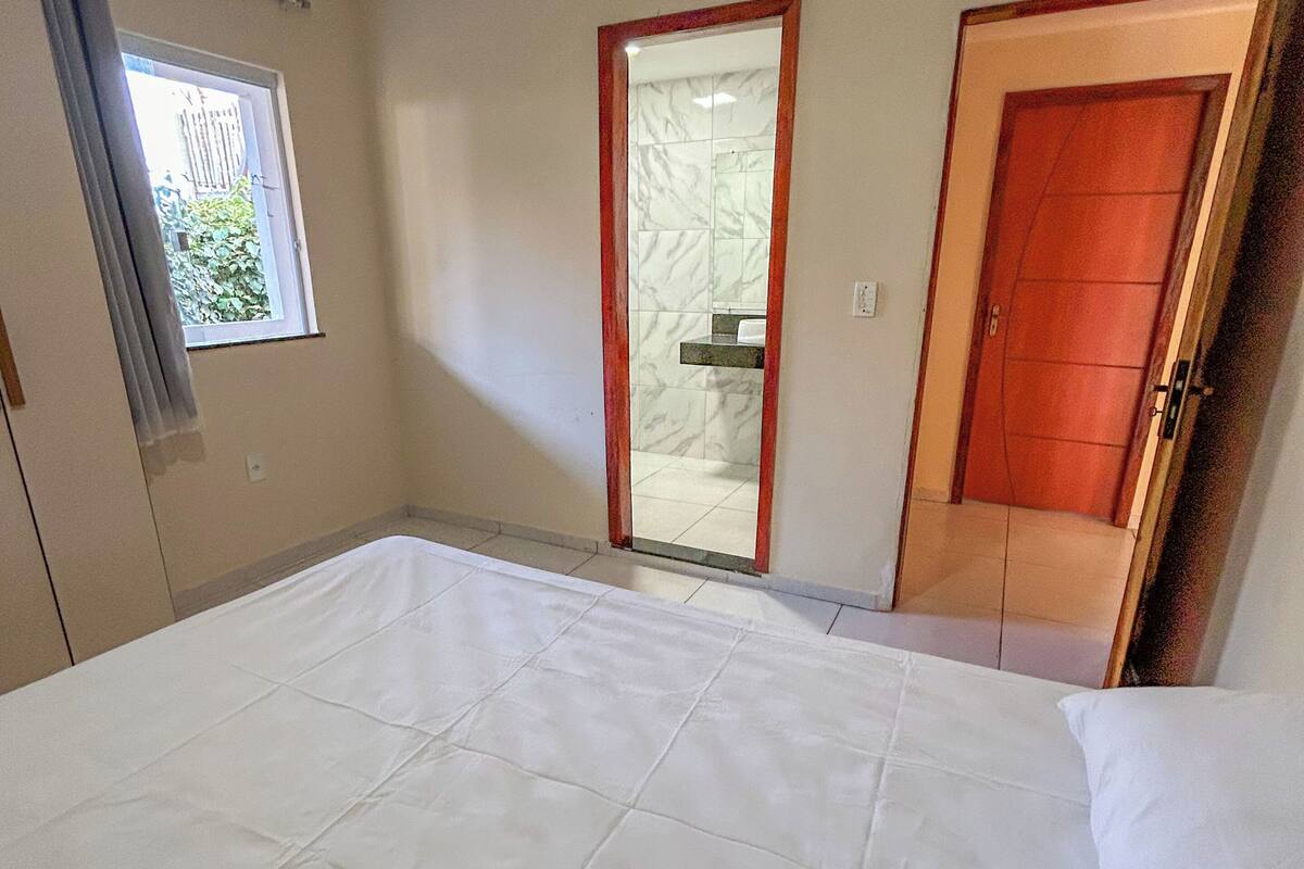 Um quarto com uma cama grande, uma janela com cortinas, uma porta e um espelho.