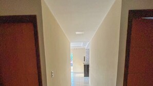 Un pasillo con paredes blancas y suelo de baldosas que conduce a una habitación con ventana.