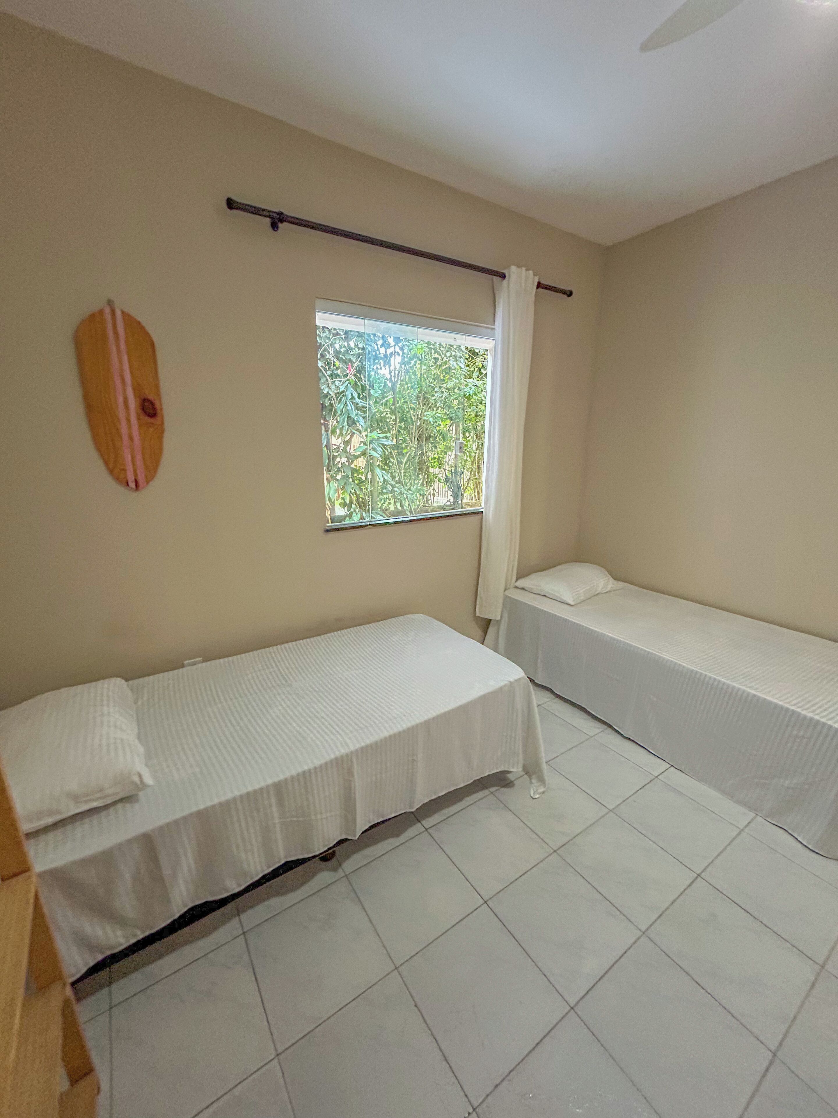 A room with two single beds, a window with a view of greenery, and a ceiling fan.