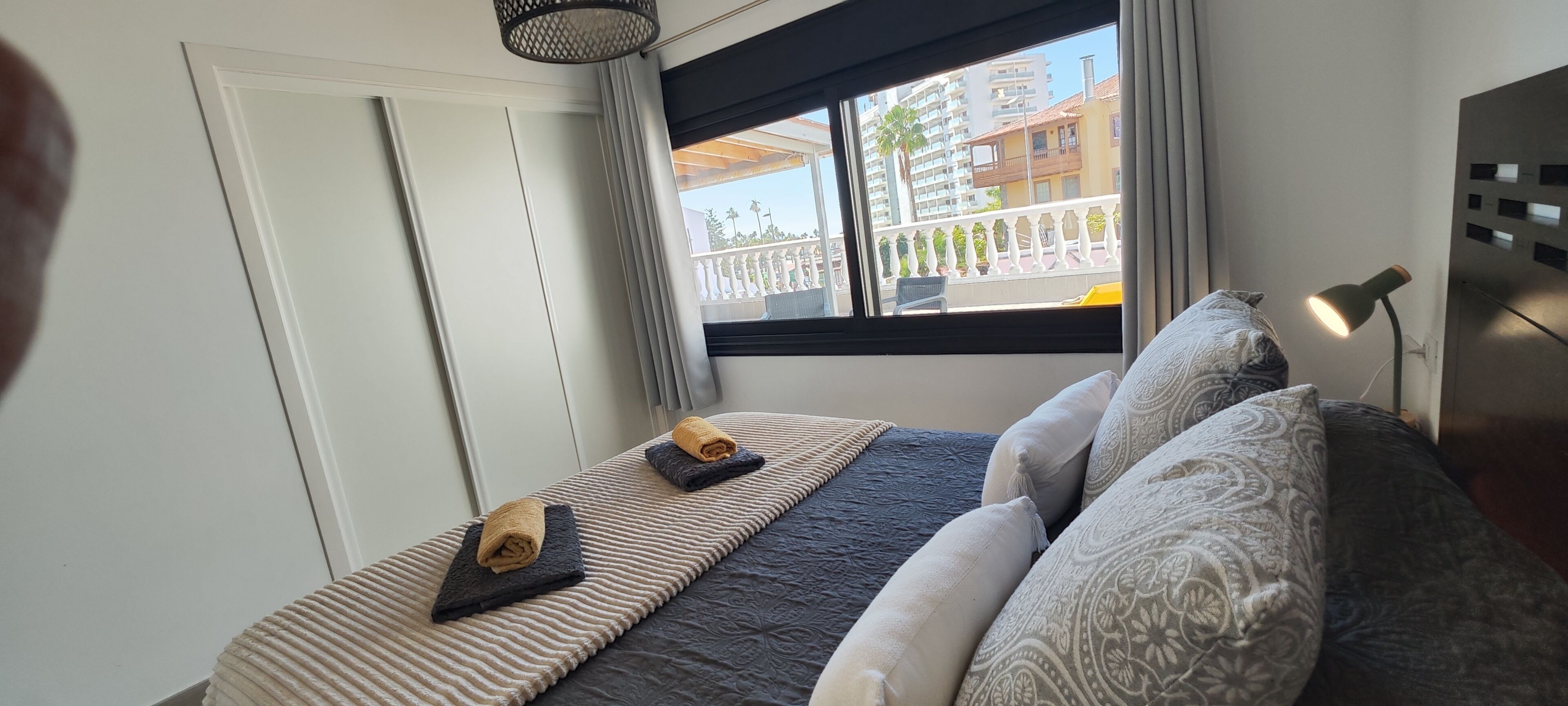 A bedroom with a bed, pillows, a window with a view of buildings, a lamp, and a door.