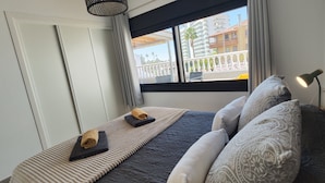 Ein Schlafzimmer mit Bett, Kissen, einem Fenster mit Blick auf Gebäude, einer Lampe und einer Tür.