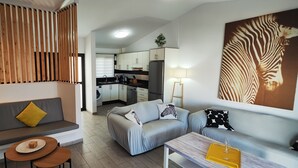 Ein moderner Wohnbereich mit Sofa, Couchtisch, Esstisch und einer Küche im Hintergrund. An der Wand hängt ein Zootier-Kunstwerk, das ein Zebra zeigt.