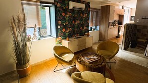 A modern living room with a wooden floor, a dining area with a wooden table and yellow chairs, a potted plant, and a kitchen in the background. - Le diX - Classic Room - Vallabrix (Vallabrix)