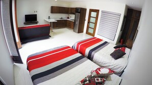 Une chambre avec deux lits, une petite kitchenette, une télévision et un ventilateur de plafond.