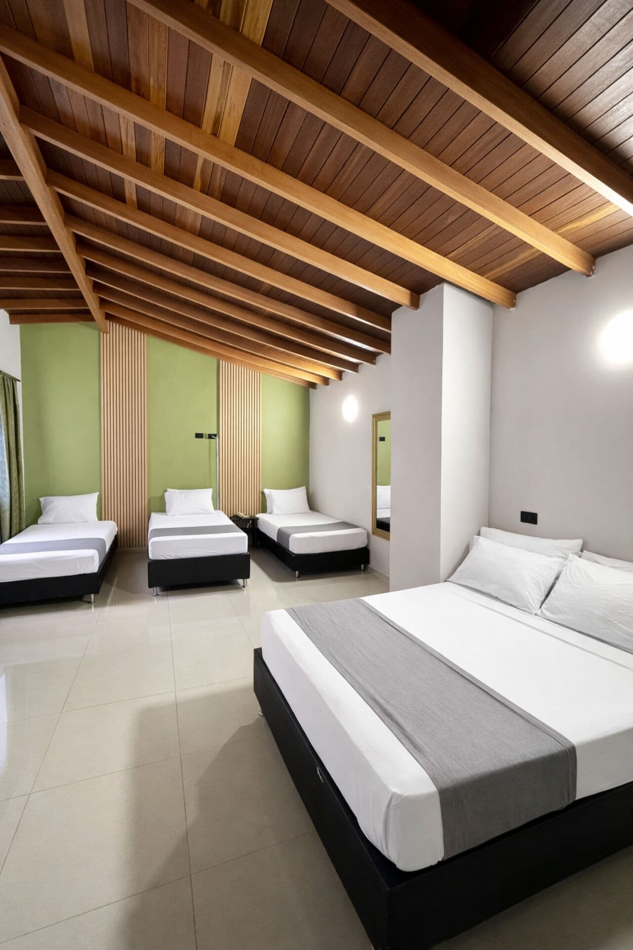 Une chambre d’hôtel moderne avec un plafond en bois, trois lits et des murs verts.