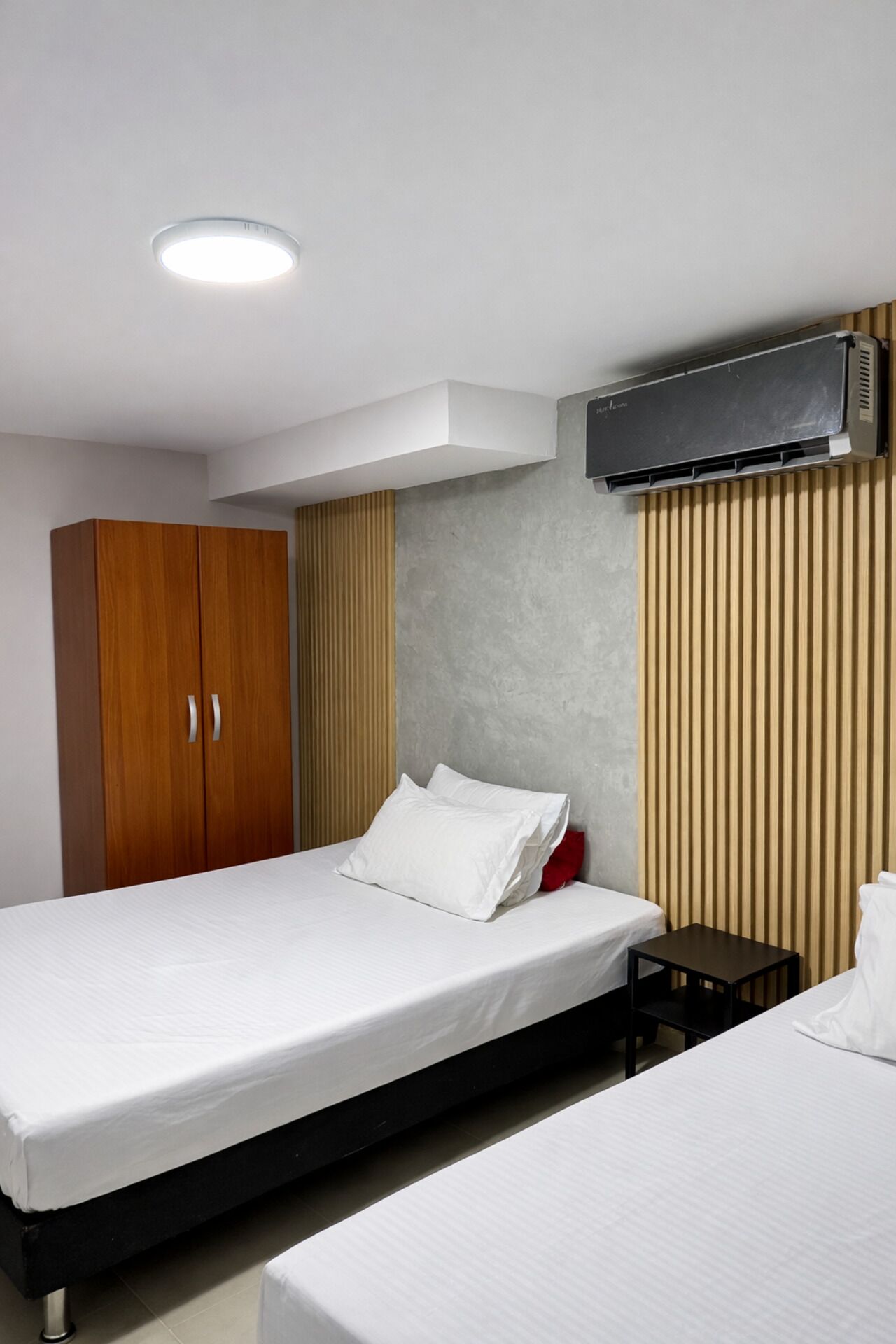 A hotel room with a bed, a wardrobe, a bedside table, and a wall-mounted air conditioner.