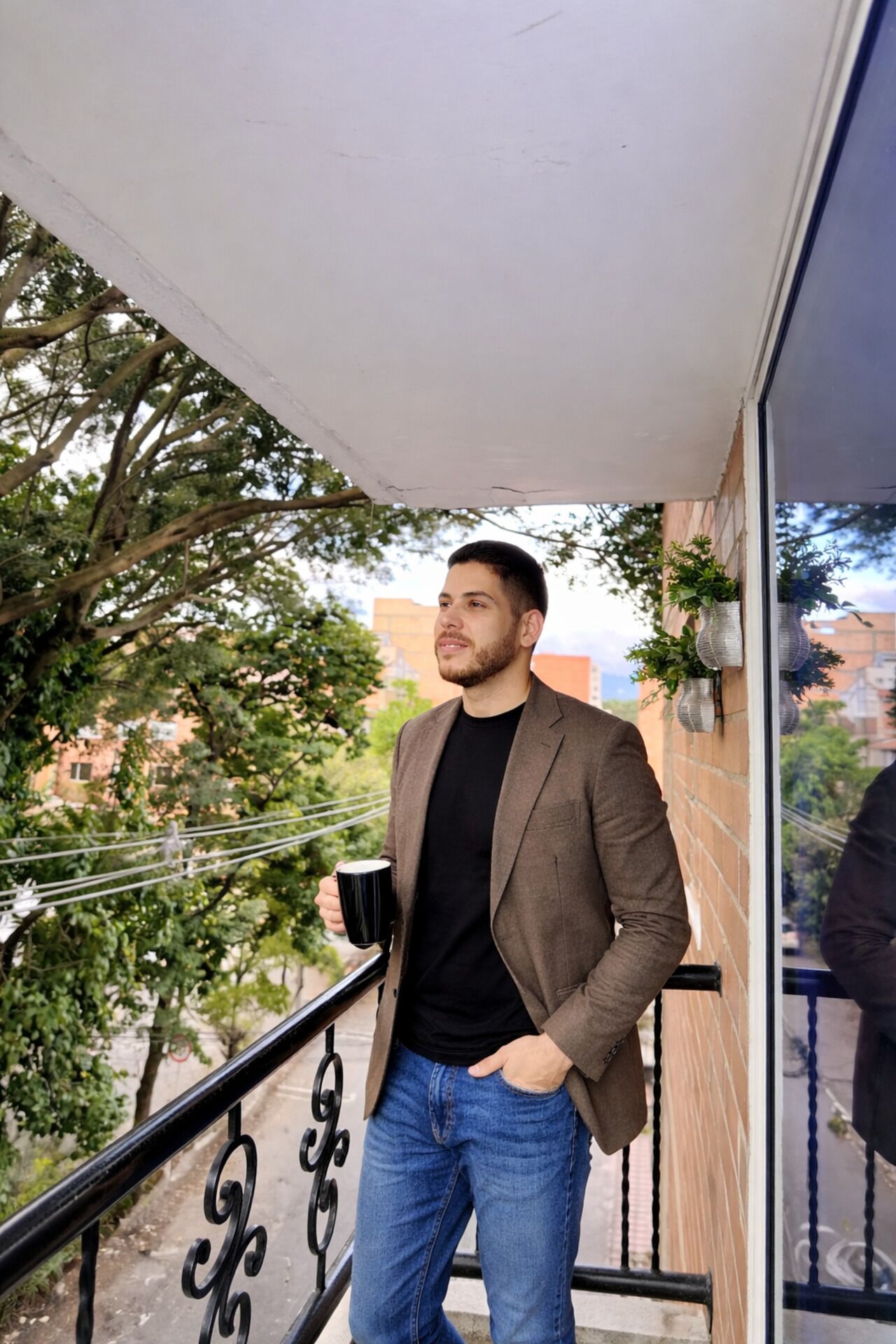 A man standing on a balcony with a railing, holding a black mug.