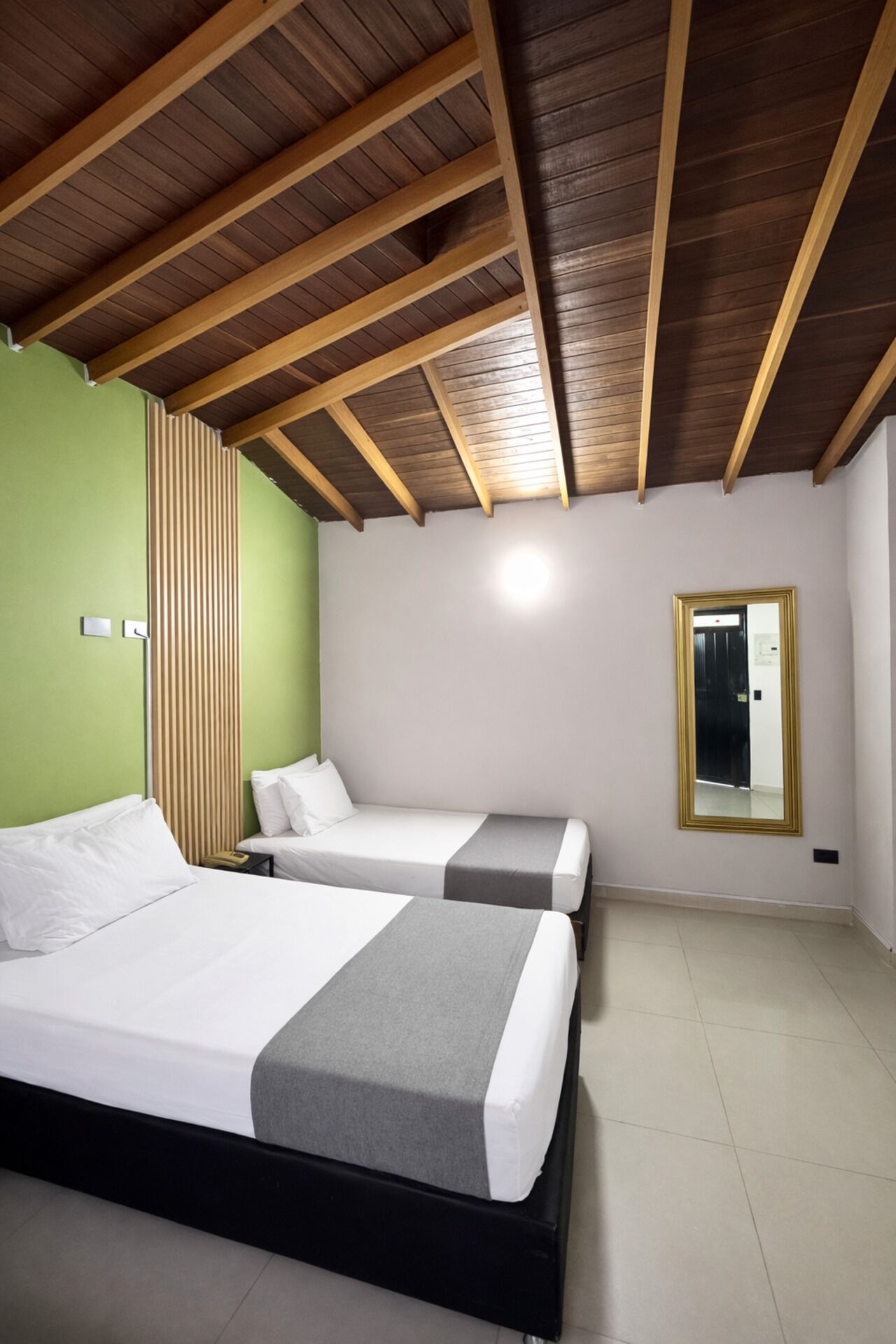 A room with two beds, a wooden ceiling, a green wall, and a mirror.