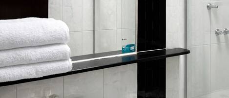 Un baño moderno con estante de vidrio, lavamanos blanco, inodoro y espejo.