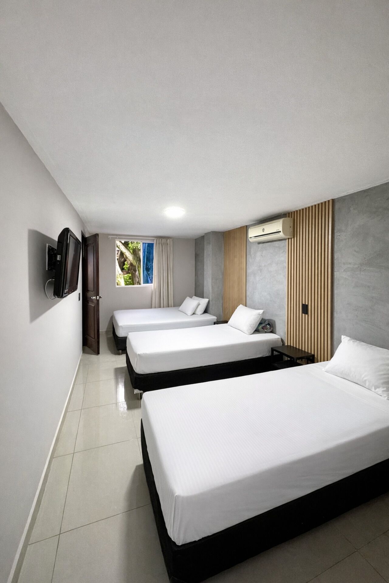 A hotel room with three beds, a TV, and an air conditioning unit.