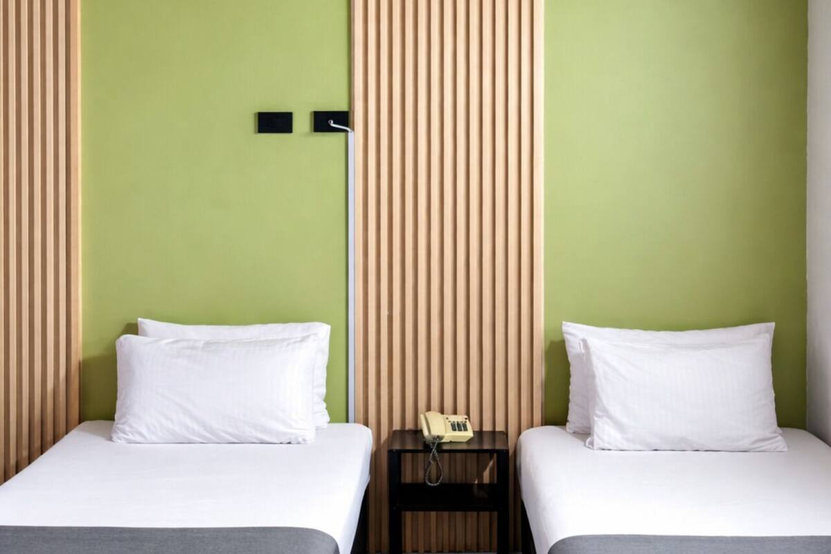 A room with two beds, a wooden ceiling, and a green wall.