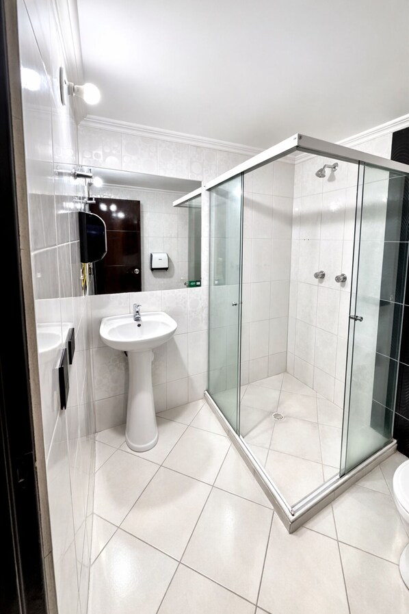 Un baño moderno con ducha de mampara de vidrio, lavamanos pedestal y retrete.