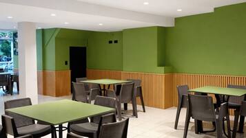 Un comedor moderno con paredes verdes, varias mesas y sillas.