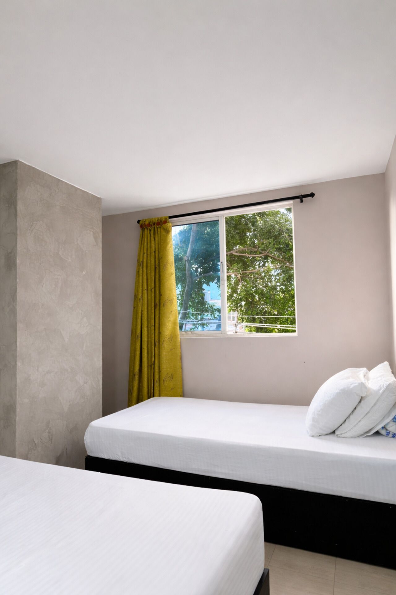 Une chambre avec un lit simple, une fenêtre avec un rideau et une vue sur les arbres à l’extérieur.