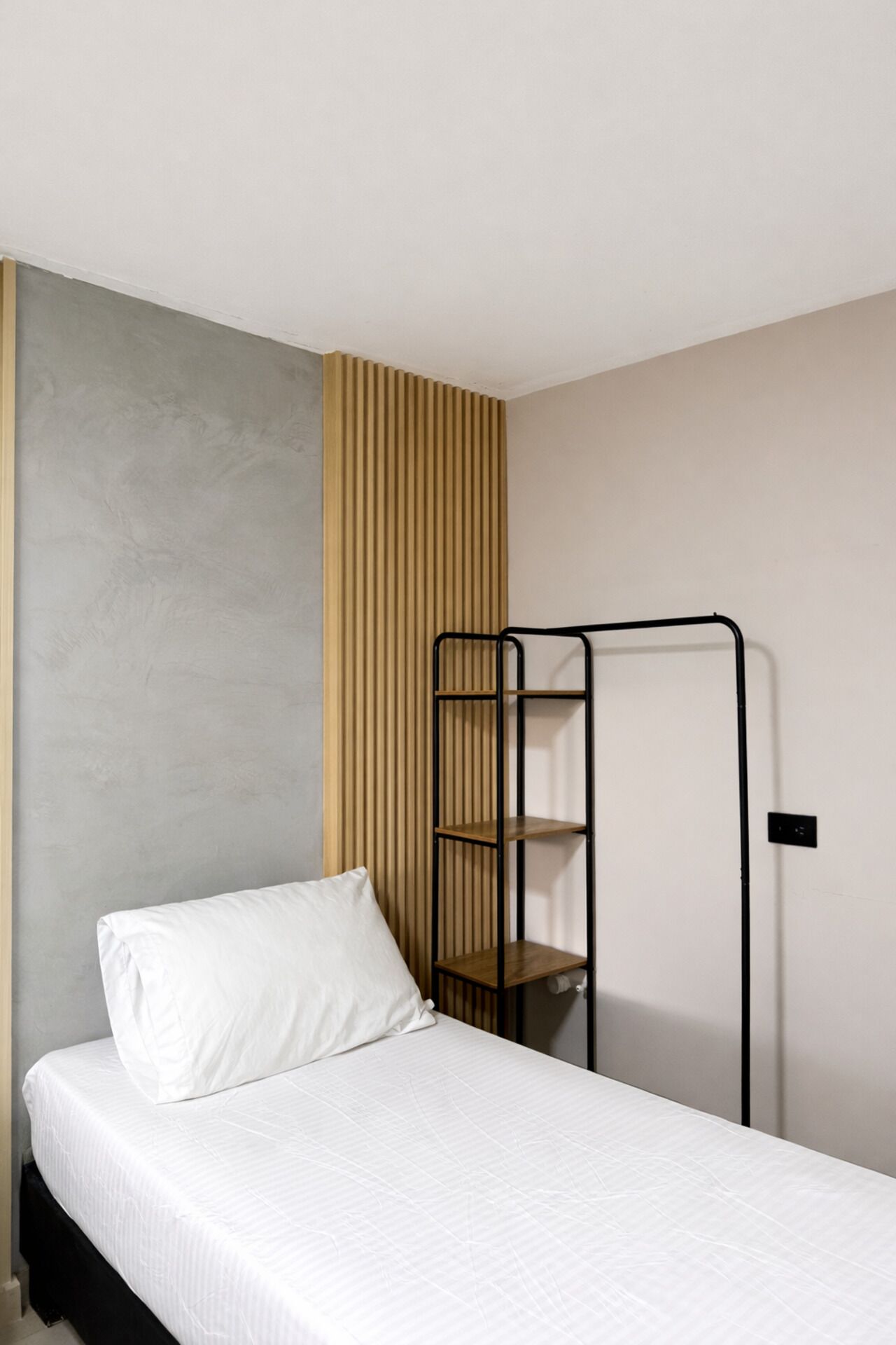 Een eenpersoonsbed met een witte matras en kussen, een zwarte metalen trap en een houten paneel met latten.