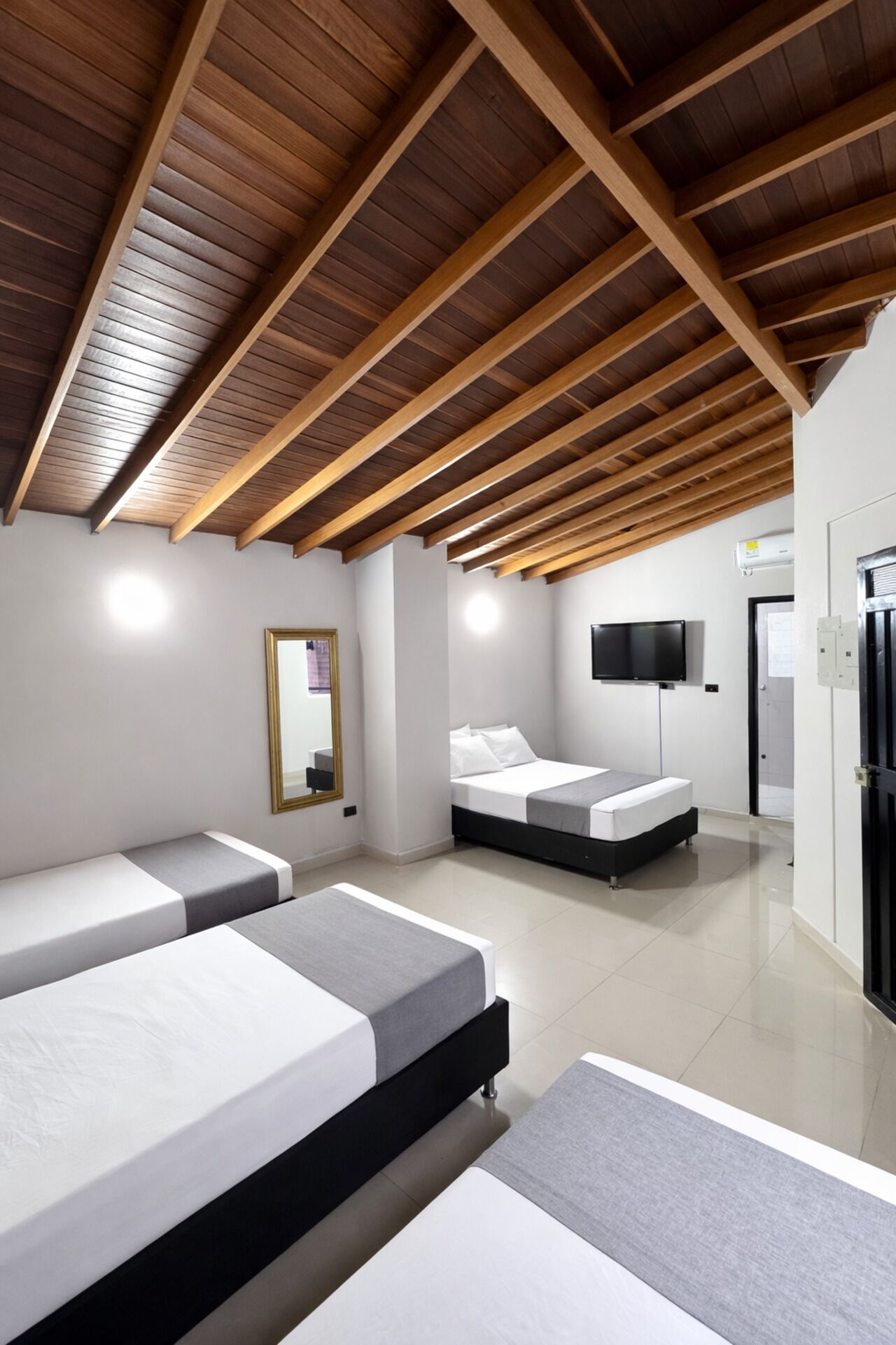 Quarto moderno com teto inclinado, duas camas, uma TV de tela plana e um espelho.