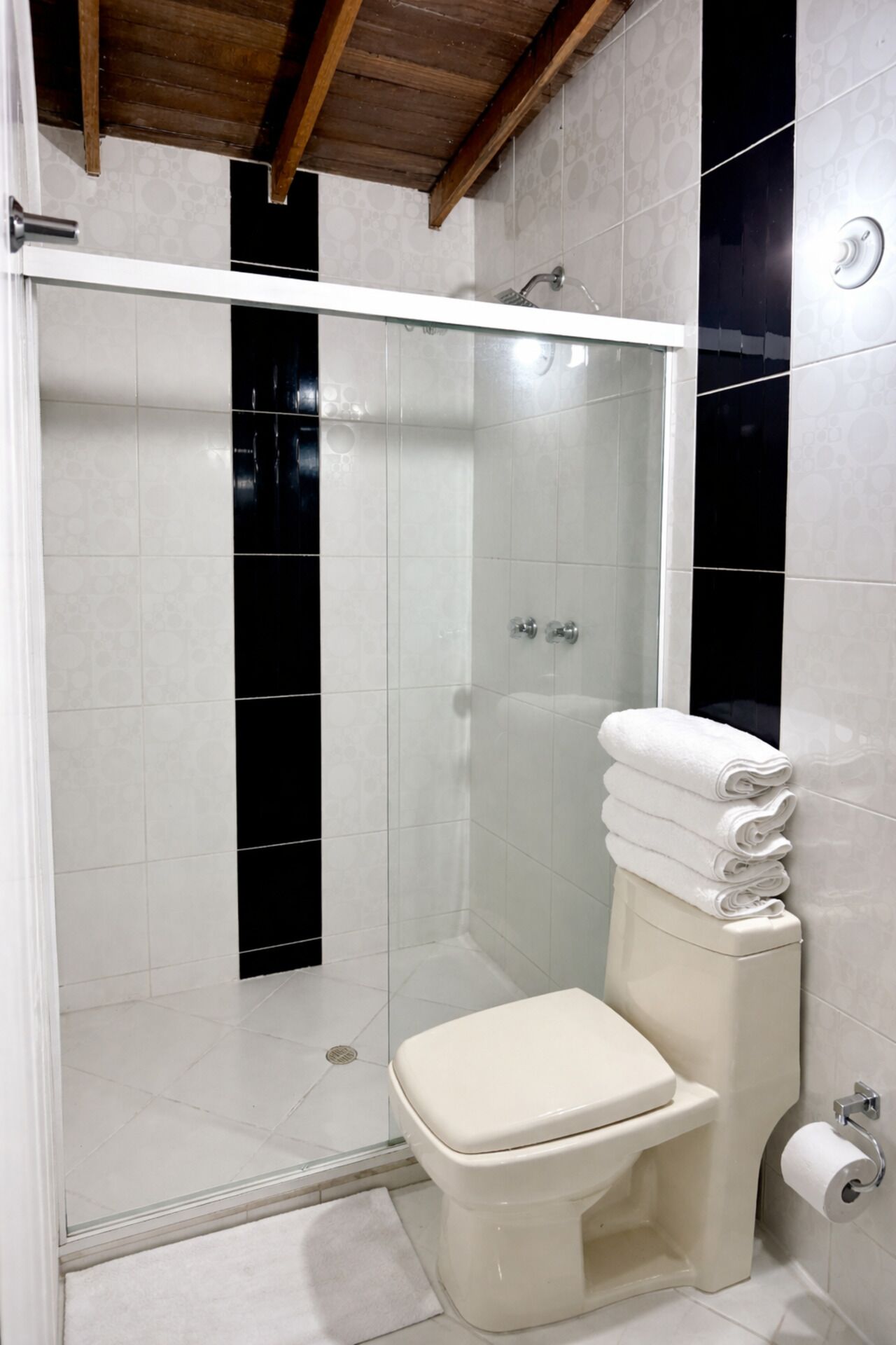 Et badeværelse med brusebad, toilet og en stak hvide håndklæder.