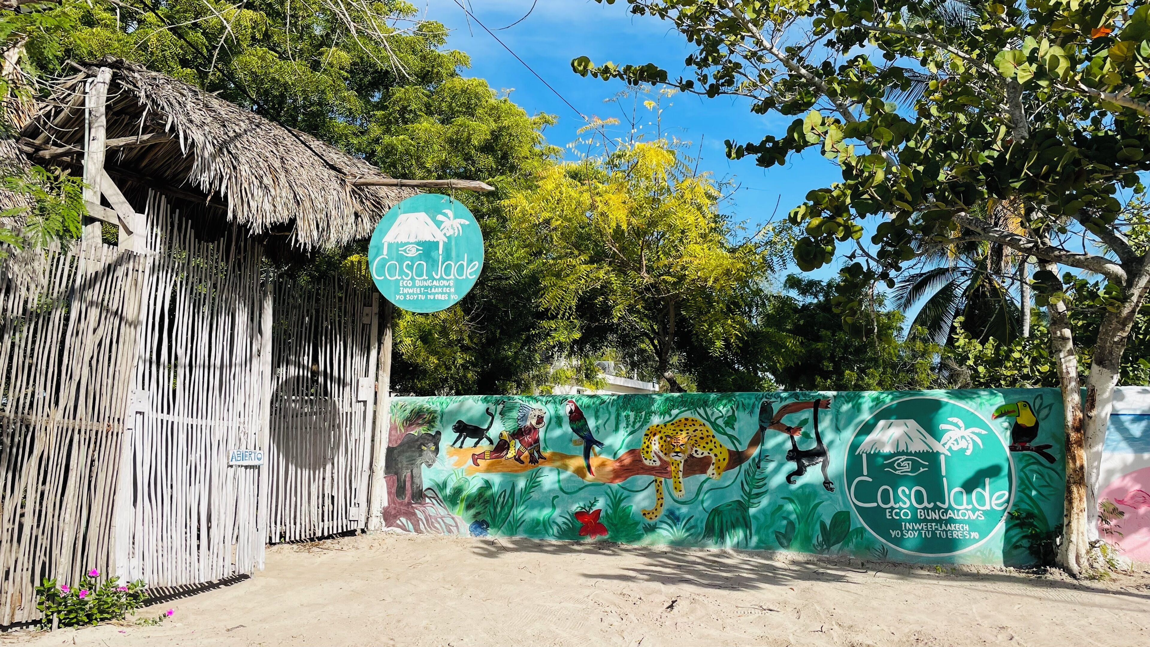 Une cabane rustique en bois, dotée d’un toit de chaume, une enseigne indiquant les « éco-bungalows Casa Jade », et une fresque représentant la faune tropicale sur une clôture.