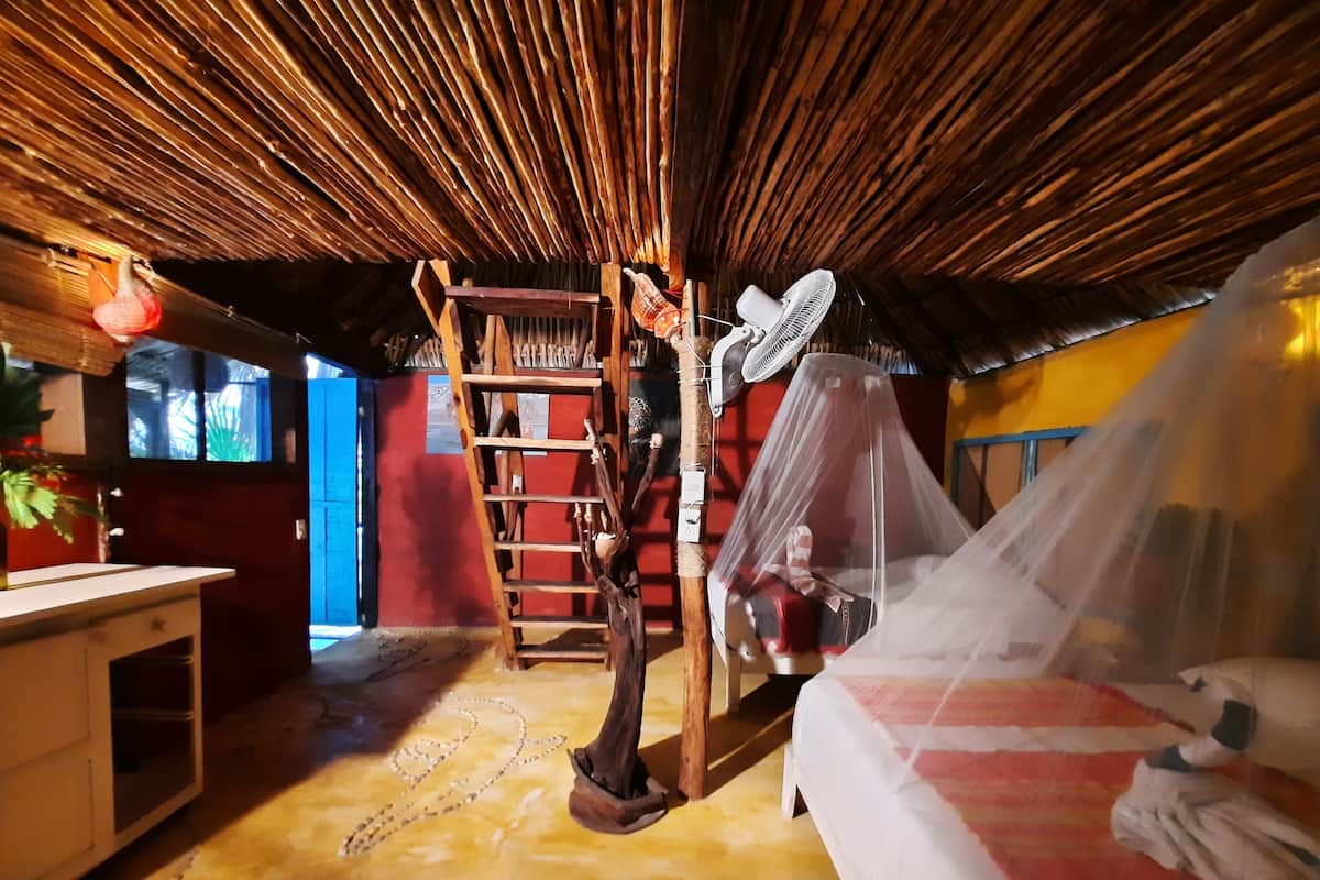 Una habitación con techo de madera, una cama con mosquitera, un escritorio y una escalera.