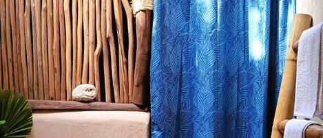 Un baño con pared de madera, cortina de ducha azul estampada, lavabo de piedra, una botella de jabón líquido y un perchero para toallas.