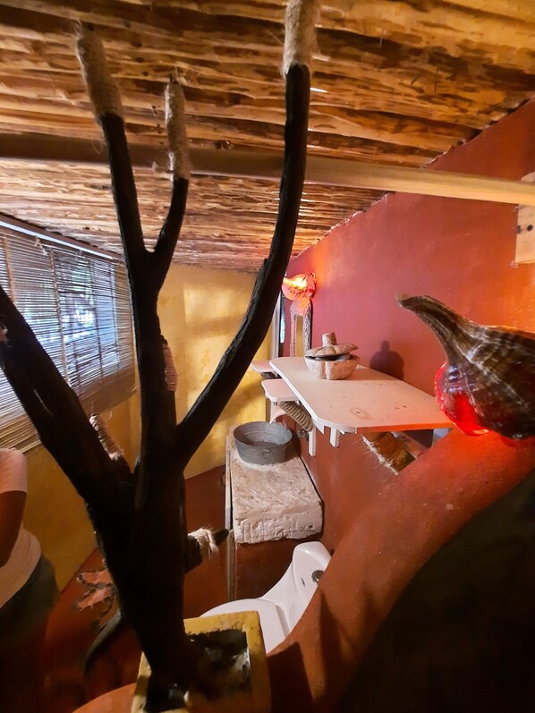 A rustic interior with a wooden ceiling, a window with blinds, a wooden table, and a ceramic pot. - Casa Jade coloradas (Río Lagartos)