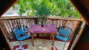 Une pièce hexagonale dotée d’un plancher en bois, d’un tapis aux motifs rouges et blancs, de deux chaises bleues, d’une table recouverte d’une nappe à rayures et d’une plante en pot ornée de fleurs rouges.