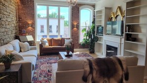 A living room with a fireplace, a sofa, a coffee table, and a dog. - Historic Downtown St Marys Loft Experience (Saint Marys)