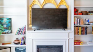 A living room with a fireplace, a mounted TV, and bookshelves filled with books and decorative items. - Historic Downtown St Marys Loft Experience (Saint Marys)