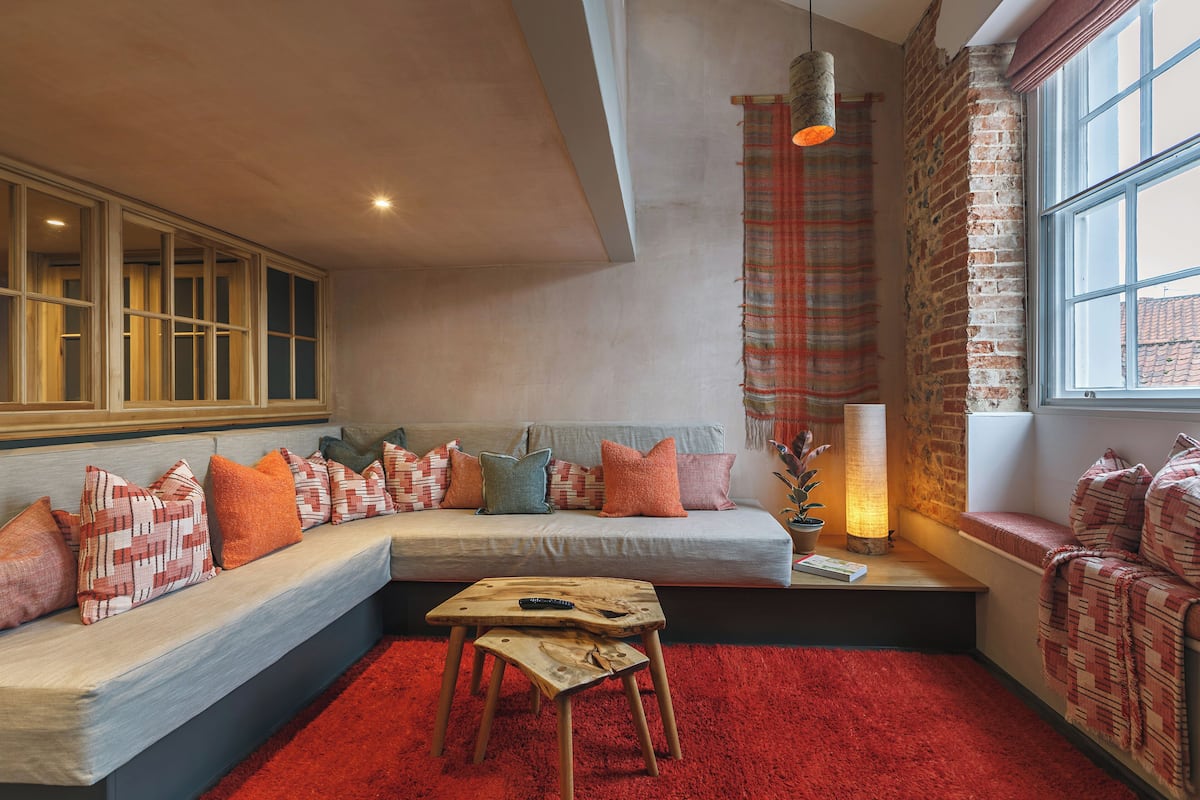 A cozy living room with a sectional sofa, a small wooden table, and a red carpet.