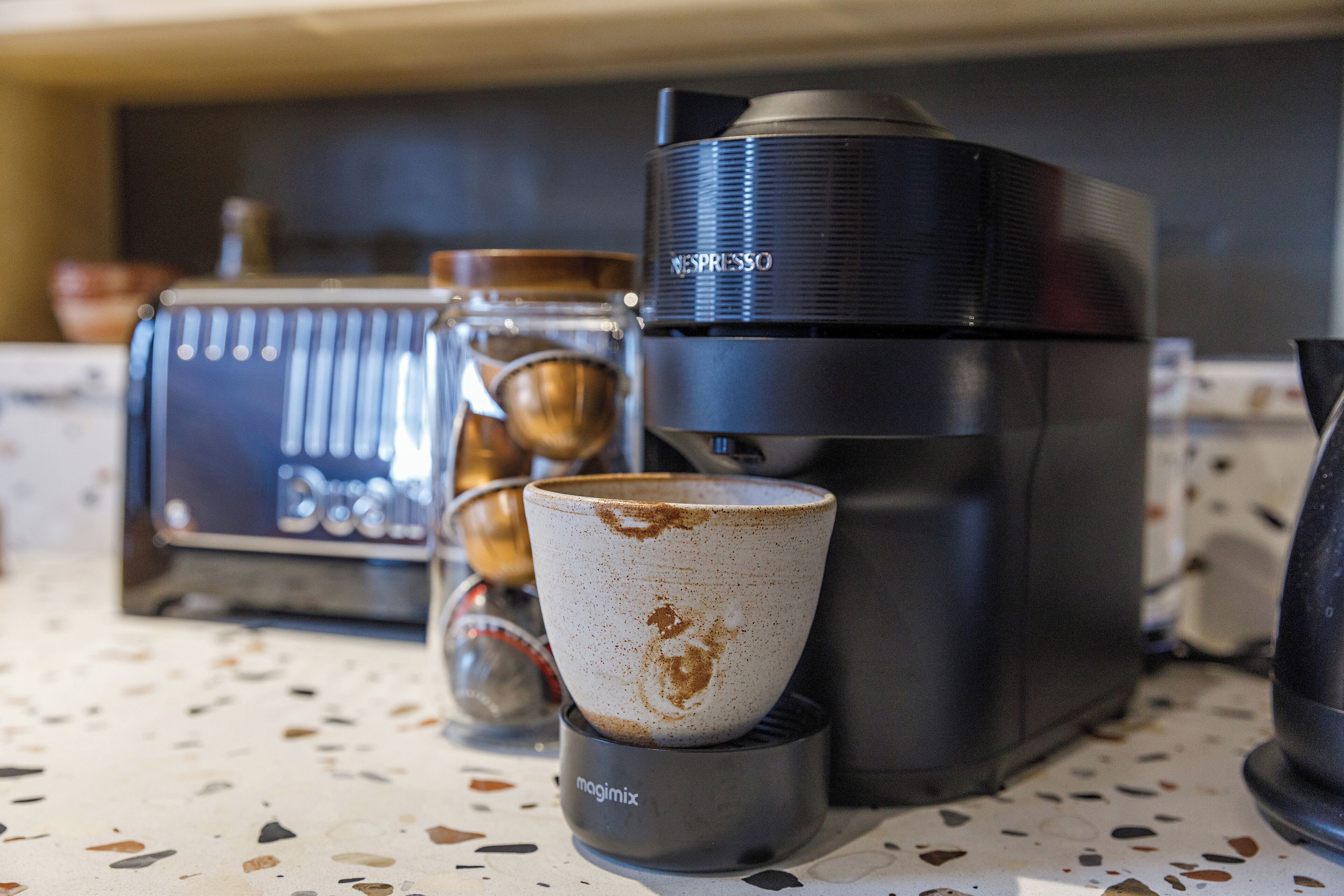 Eine Kaffeemaschine, eine Tasse und eine Waage auf einer Arbeitsplatte.