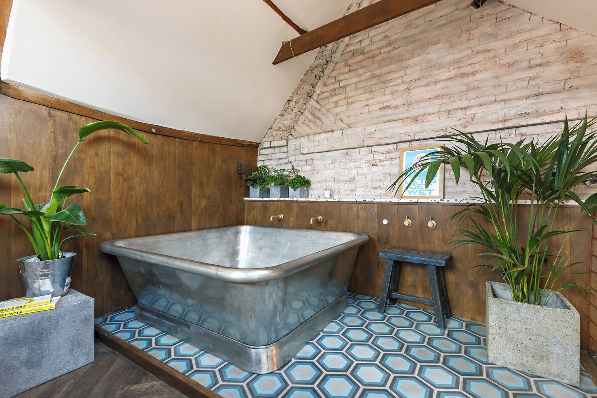 A bathroom with a large bathtub, wooden walls, and a brick ceiling. There are potted plants and a small stool.