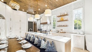 A modern kitchen with white cabinetry, a wooden ceiling, pendant lights, a large island with seating, and a window providing natural light. - Dreamy retreat—5-min to beach, private pool, LSV, & home theater | Sleeps 20! (Seagrove Beach)