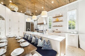 A modern kitchen with white cabinetry, a wooden ceiling, pendant lights, a large island with seating, and a window providing natural light.