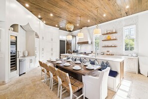 A modern kitchen with a wooden ceiling, white cabinetry, and a central island with seating.