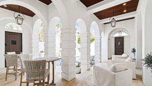 A spacious indoor area with white columns, a dining table with chairs, and a sofa. - Dreamy retreat—5-min to beach, private pool, LSV, & home theater | Sleeps 20! (Seagrove Beach)