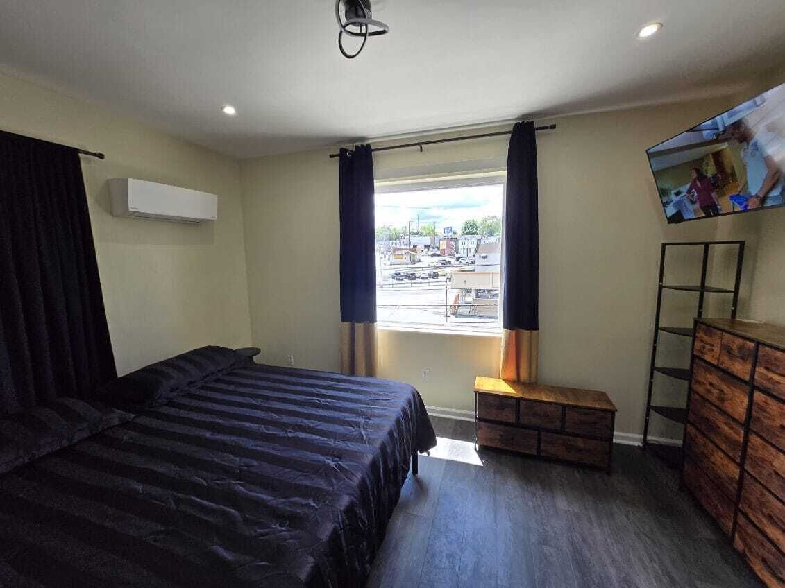 Un dormitorio con cama, ventana con cortinas, televisor en la pared y cómoda.