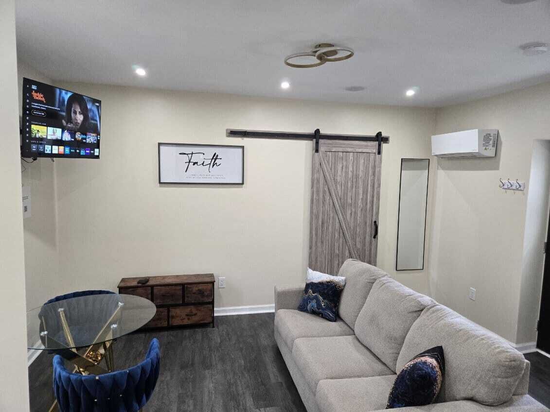 Un salon comprenant un canapé, une table basse en verre, un téléviseur fixé au mur et une œuvre d’art encadrée.