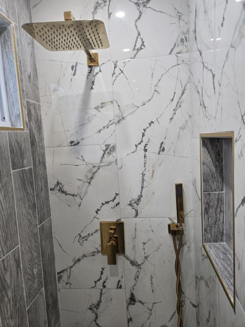 A bathroom with marble walls, a showerhead, a handheld shower, and a control panel.