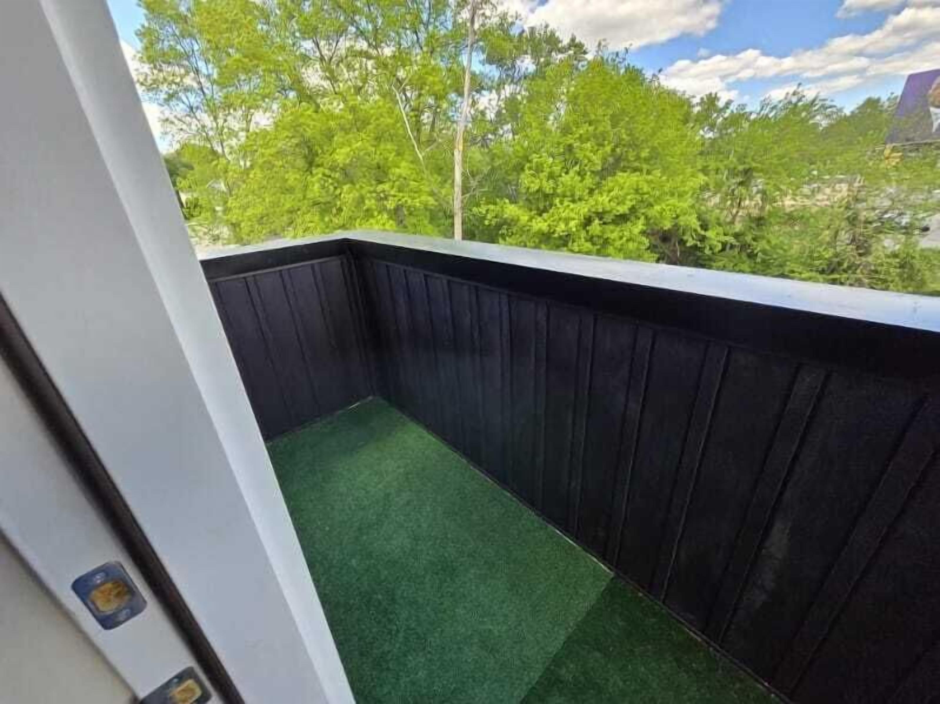 A balcony with a dark wooden railing and green artificial grass.
