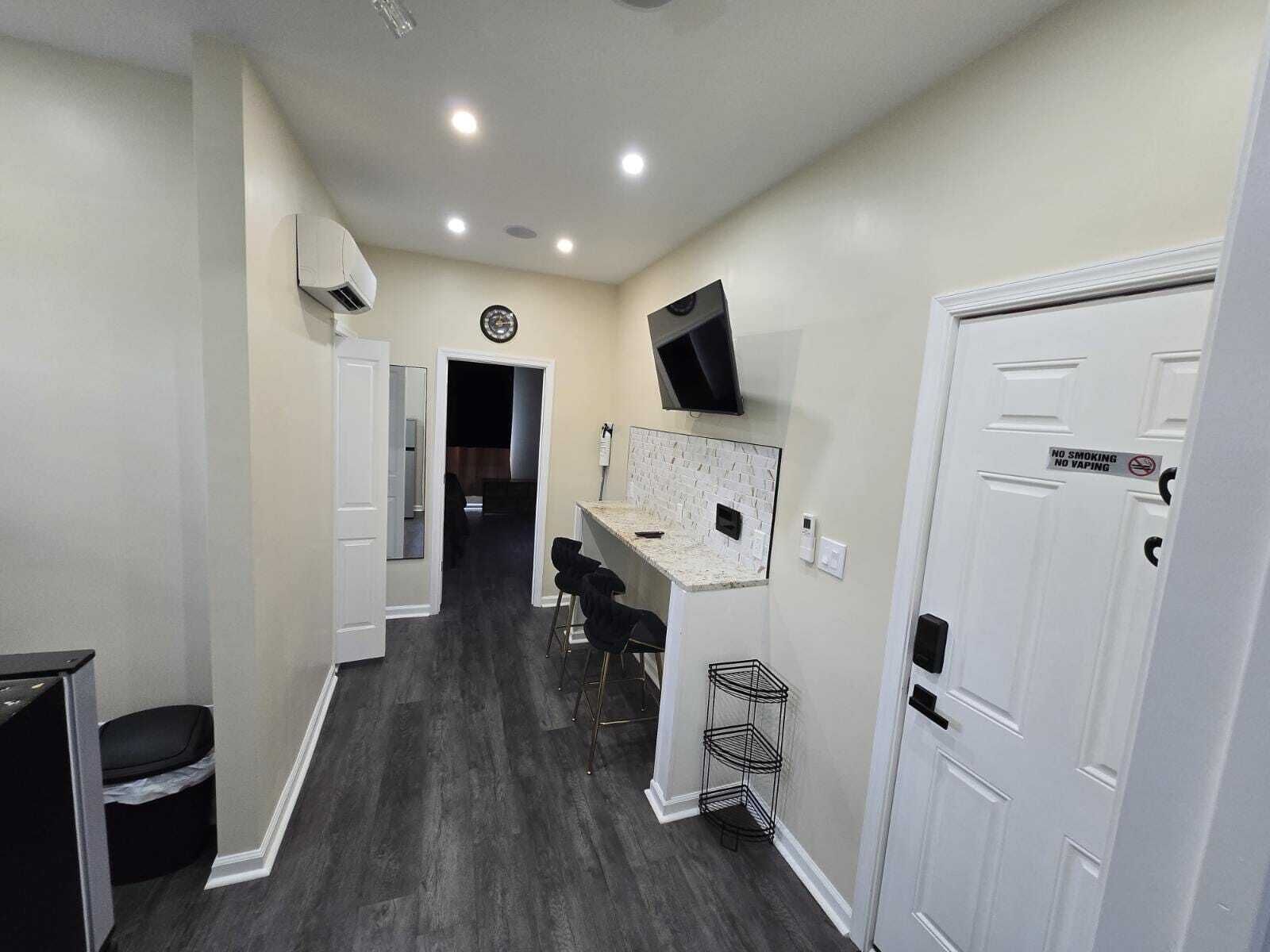 A hallway with a kitchen area, a TV mounted on the wall, and a door with a no smoking sign.