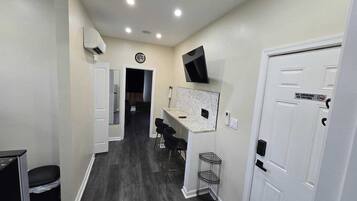 A hallway with a kitchen area, a TV mounted on the wall, and a door with a no smoking sign.