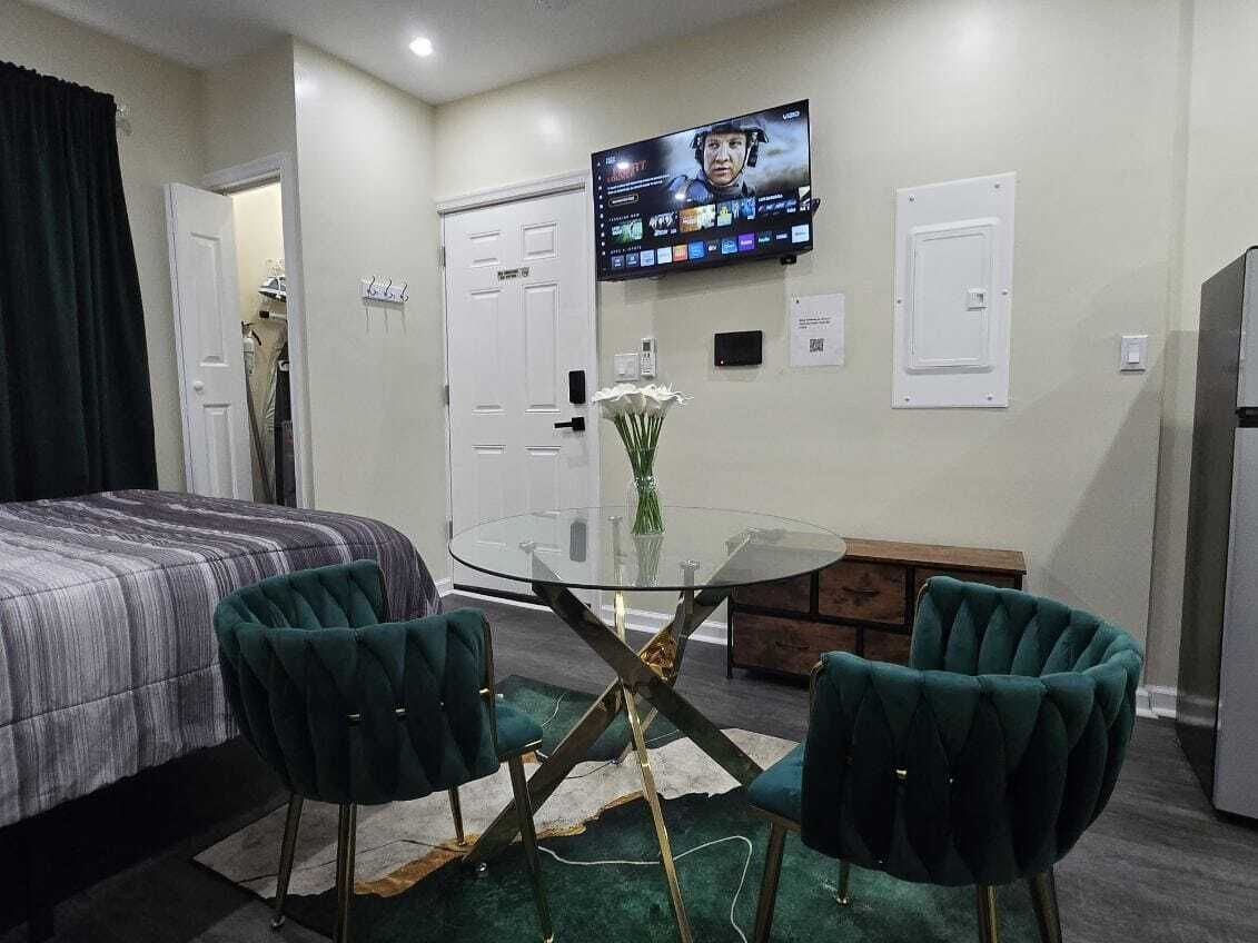 A hotel room with a bed, a round glass table with two chairs, a television mounted on the wall, and a small vase with flowers on the table.